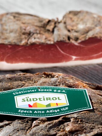 Zwei Speckseiten von originalem Südtiroler Speck auf einem Holztisch. | © Helmuth Rier